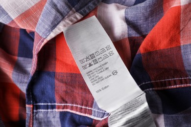 Photo of Clothing label on beautiful checkered garment, closeup