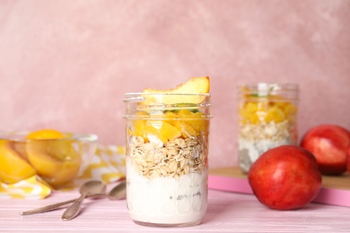 Photo of Tasty peach dessert with yogurt and granola served on pink wooden table