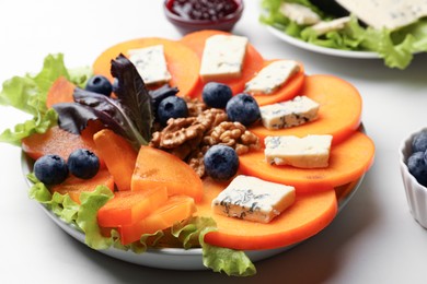 Delicious persimmon with blue cheese, blueberries, lettuce and walnuts on white table, closeup