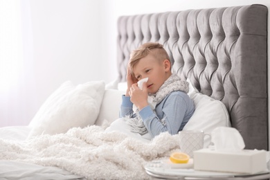 Sick little boy with tissue suffering from cold in bed