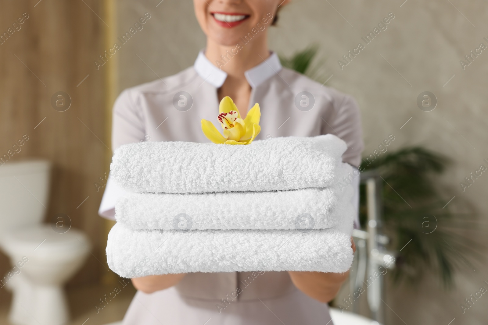 Photo of Chambermaid holding fresh towels with flower in hotel bathroom, closeup