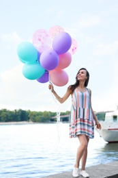 Photo of Pretty young woman with color balloons near river