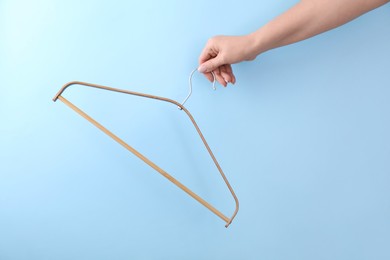 Woman holding hanger on light blue background, closeup. Space for text