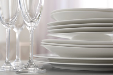 Photo of Stacked plates and glasses on light grey table, closeup
