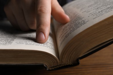 Man reading holy Bible at wooden table, closeup