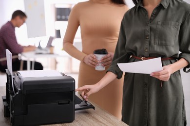 Photo of Employees using modern printer in office, closeup