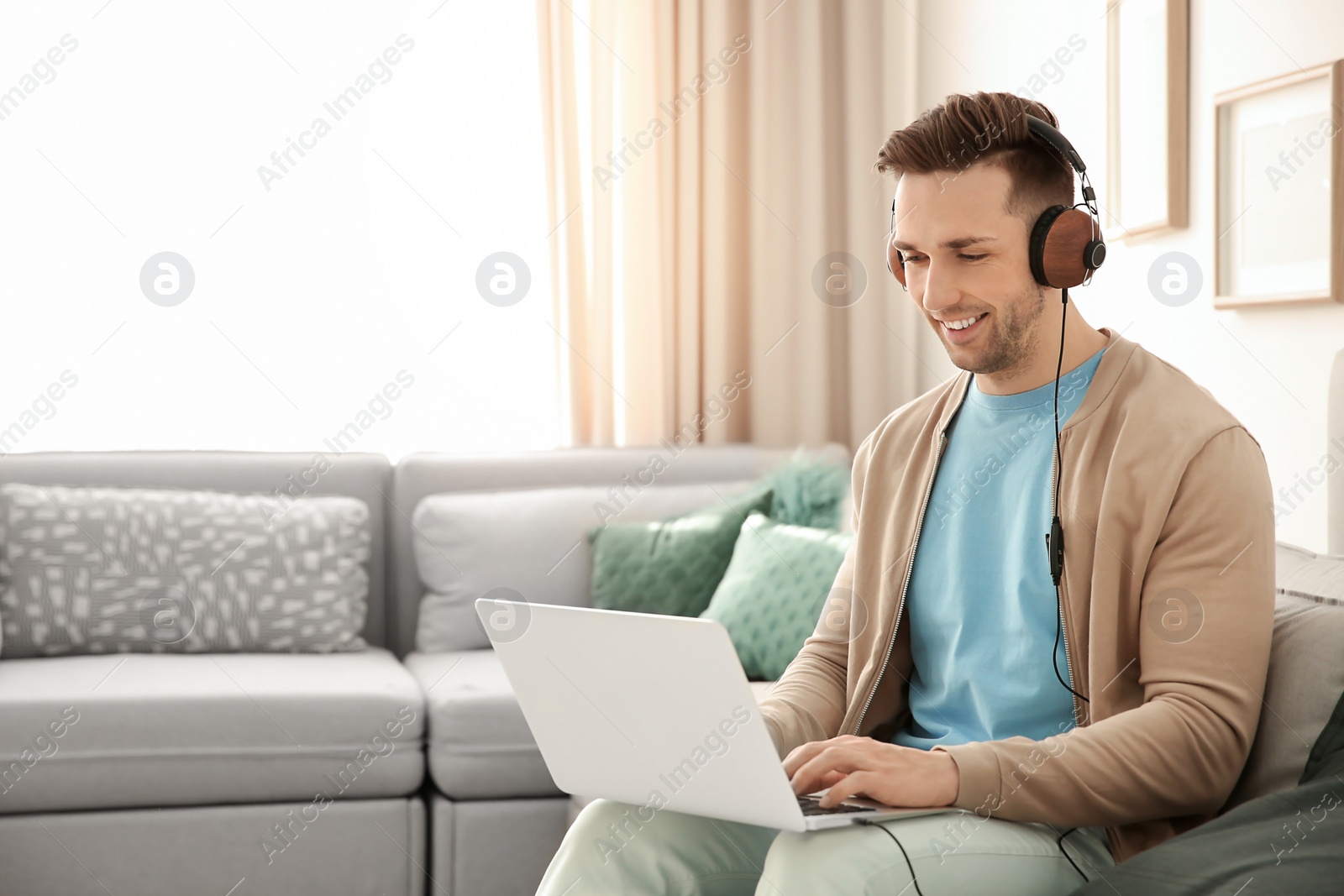 Photo of Handsome young man with laptop listening to music at home