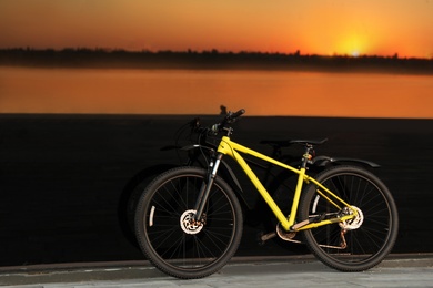 Photo of Yellow bicycle parked near glass building at sunset