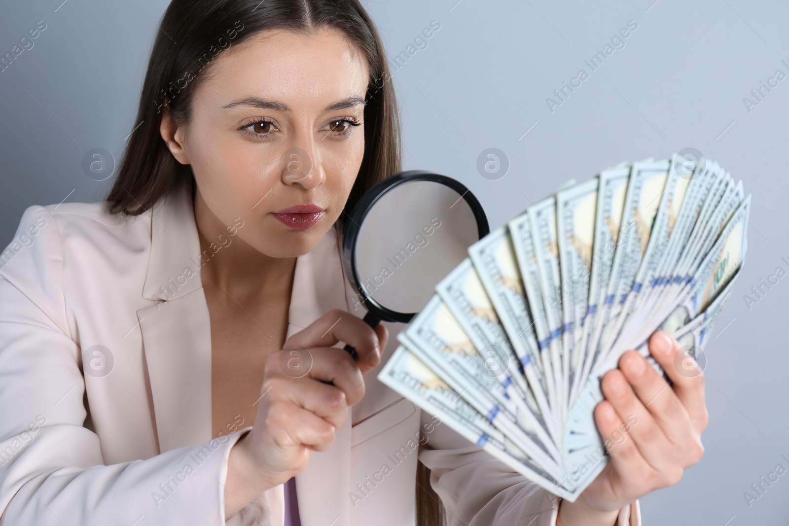 Photo of Expert authenticating 100 dollar banknotes with magnifying glass on light grey background. Fake money concept
