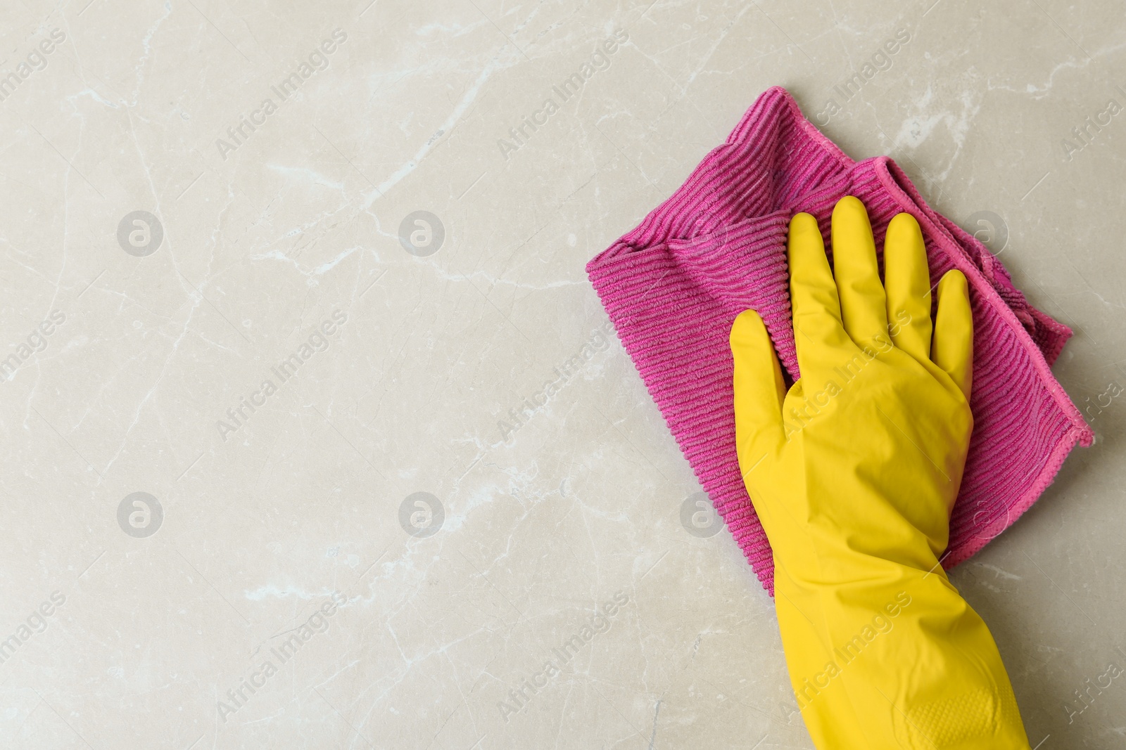 Photo of Person in gloves wiping grey marble table with rag, top view. Space for text