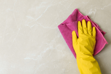 Photo of Person in gloves wiping grey marble table with rag, top view. Space for text