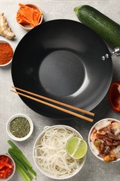 Flat lay composition with black wok surrounded by spices and products on grey textured table