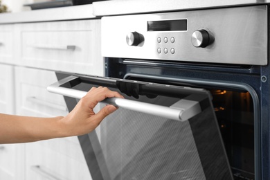 Woman opening door of oven in kitchen, closeup