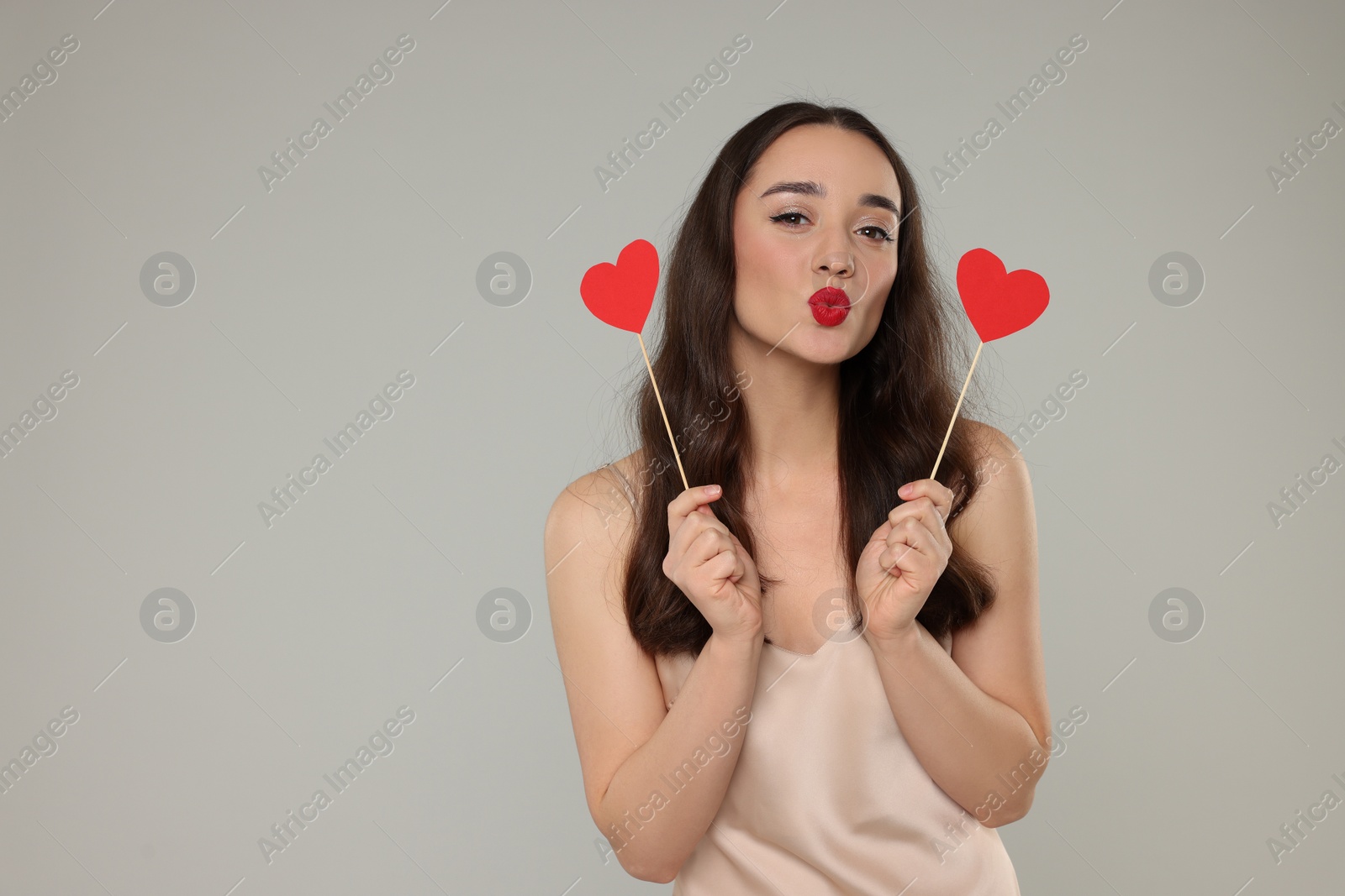 Photo of Beautiful young woman with paper hearts sending air kiss on grey background, space for text