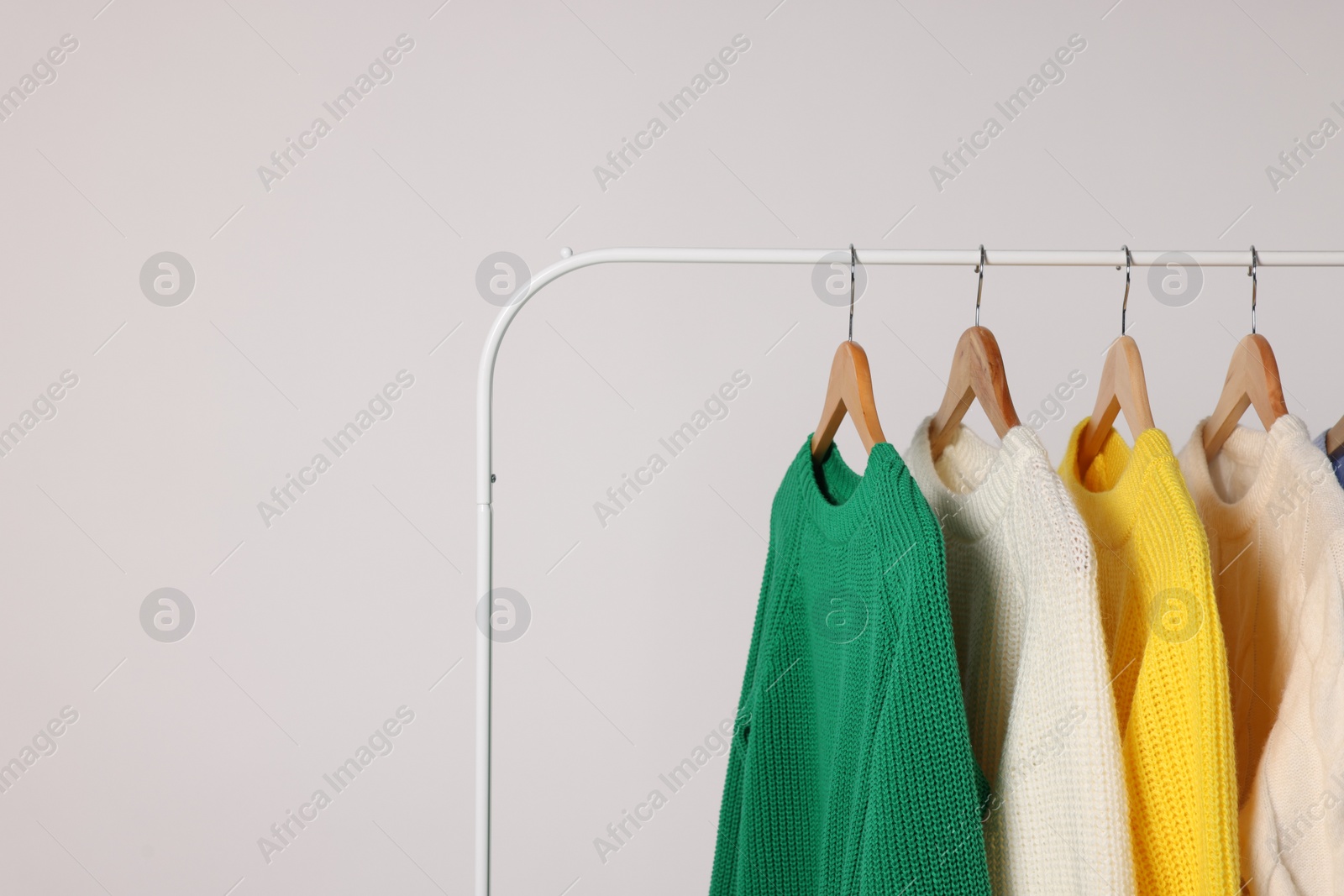 Photo of Rack with different warm sweaters on light background. Space for text