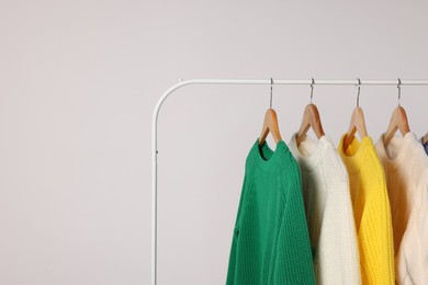 Rack with different warm sweaters on light background. Space for text