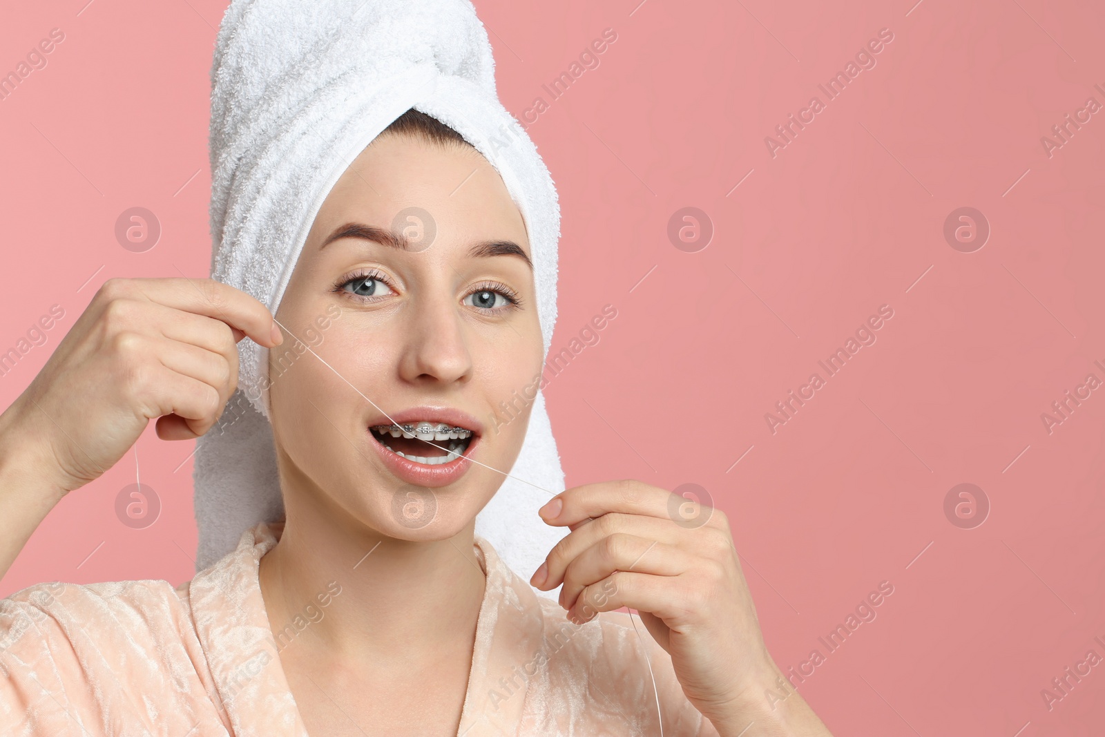 Photo of Woman with braces cleaning teeth using dental floss on pink background. Space for text