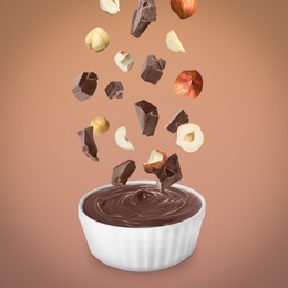 Image of Making yummy chocolate paste. Hazelnuts and pieces of chocolate falling into bowl on light brown background