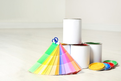 Photo of Cans of paint and color palette on wooden floor indoors