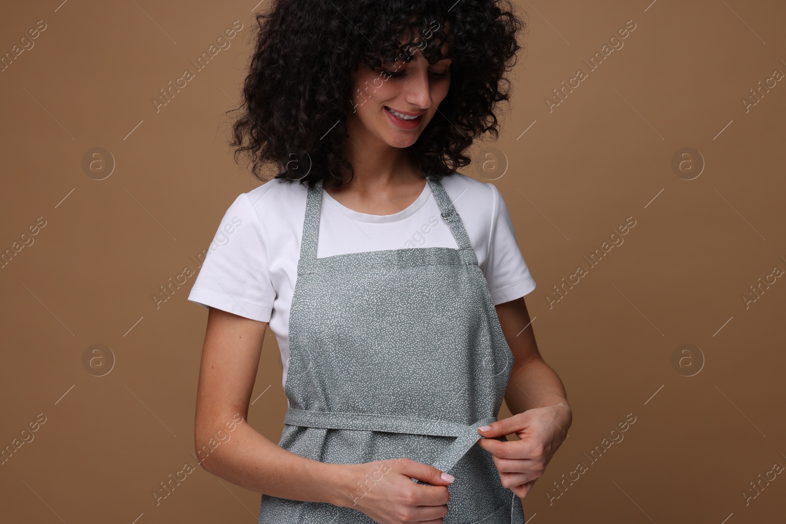 Photo of Happy woman wearing kitchen apron on brown background. Mockup for design