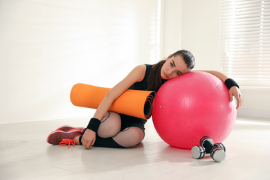 Photo of Lazy young woman with sport equipment indoors