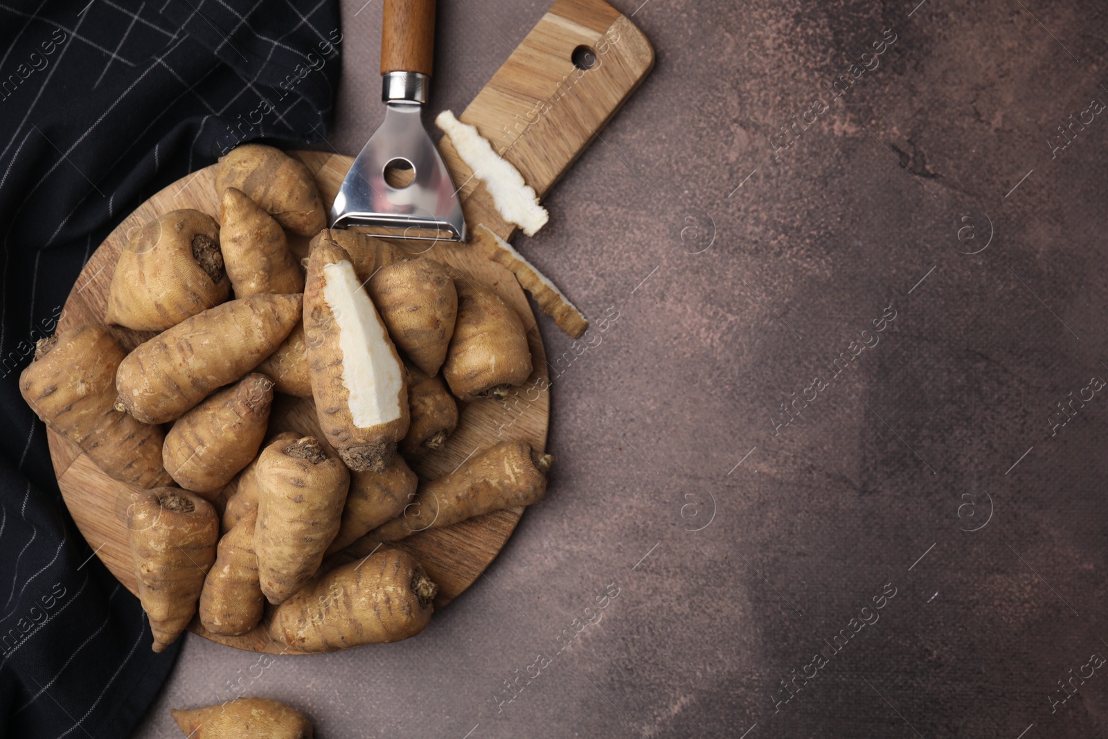 Photo of Tubers of turnip rooted chervil and peeler on brown table, top view. Space for text