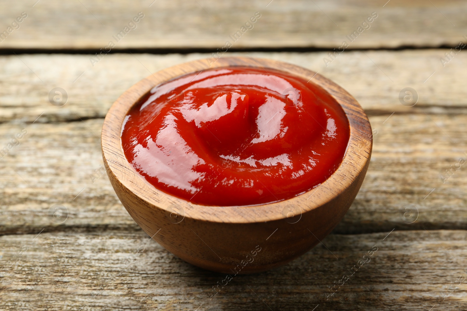 Photo of Tasty ketchup in bowl on wooden table. Tomato sauce