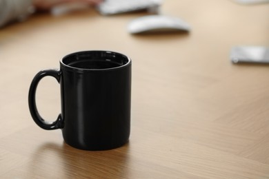 Photo of Black ceramic mug on wooden table at workplace. Space for text