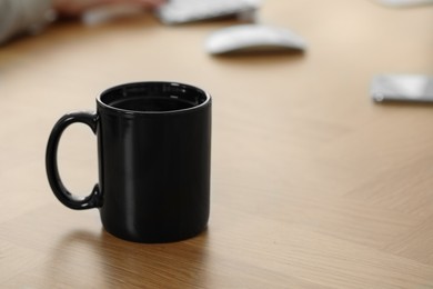 Black ceramic mug on wooden table at workplace. Space for text