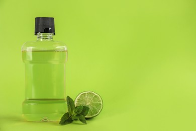 Photo of Mouthwash, fresh mint and lime on light green background. Space for text