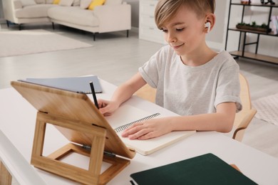 Boy in earphones doing homework with tablet at table indoors