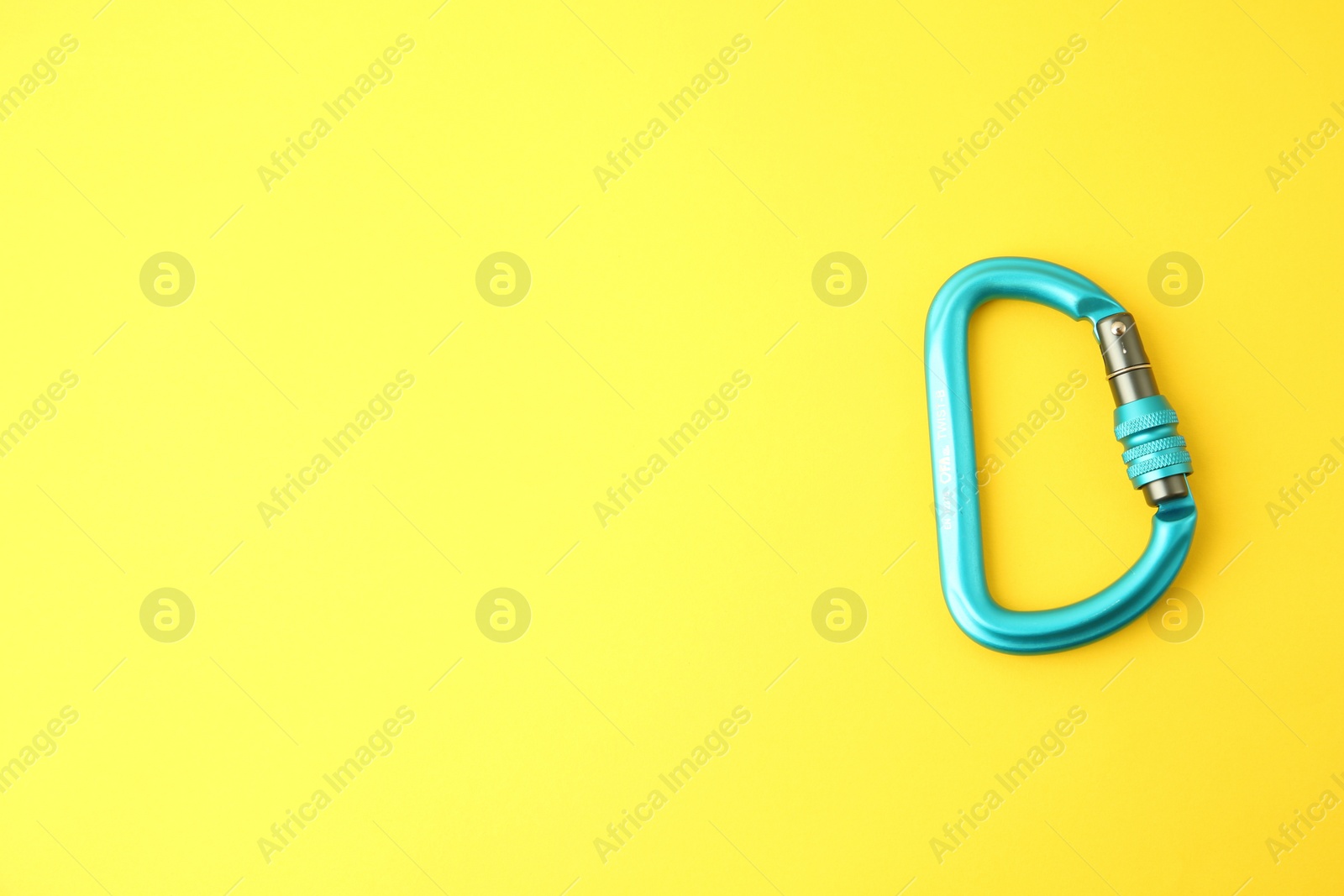 Photo of One light blue carabiner on yellow background, top view. Space for text