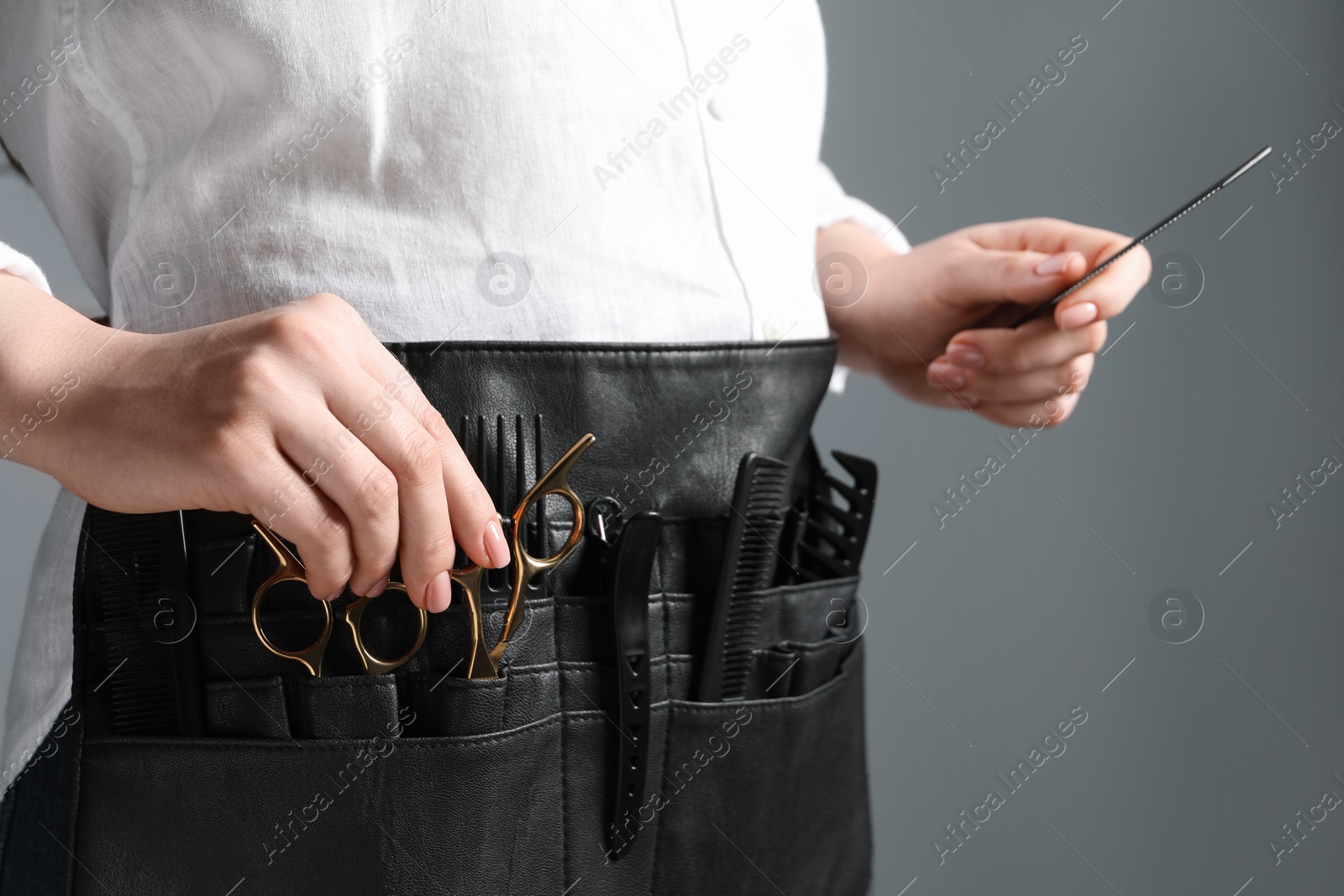 Photo of Hairstylist with professional tools in waist pouch on grey background, closeup