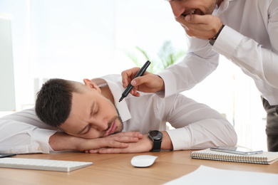 Photo of Man drawing on colleague's face while he sleeping at workplace. April fool's day