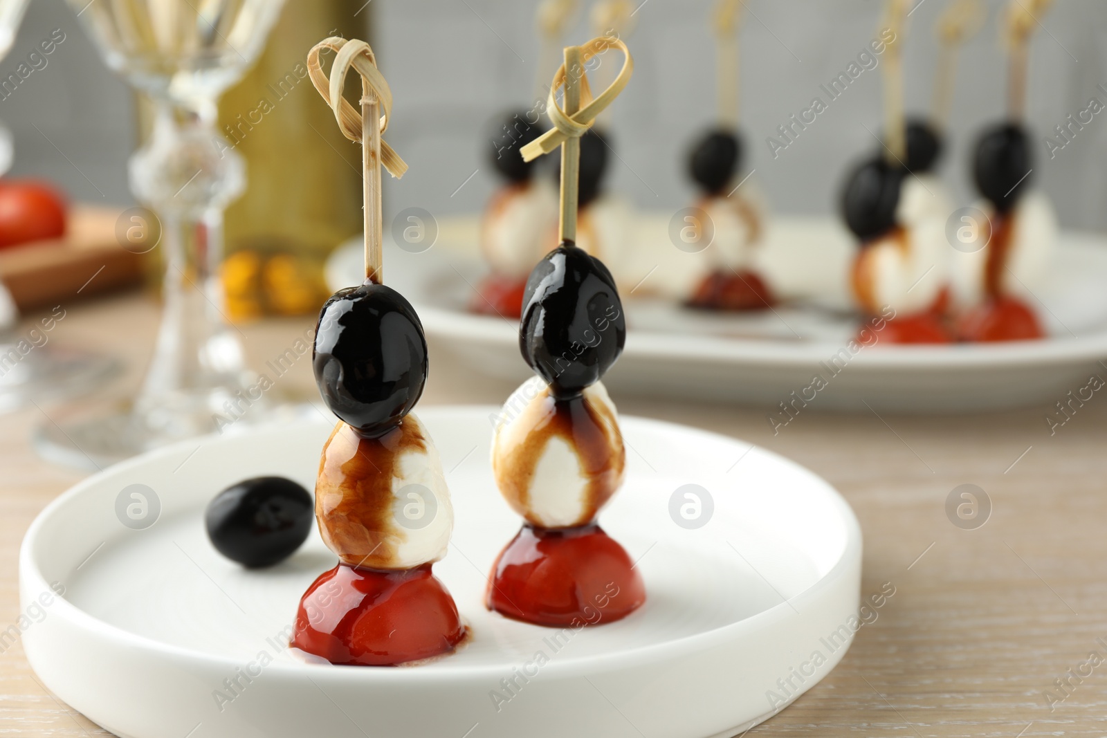 Photo of Tasty canapes with black olives, mozzarella and cherry tomatoes on light wooden table, closeup