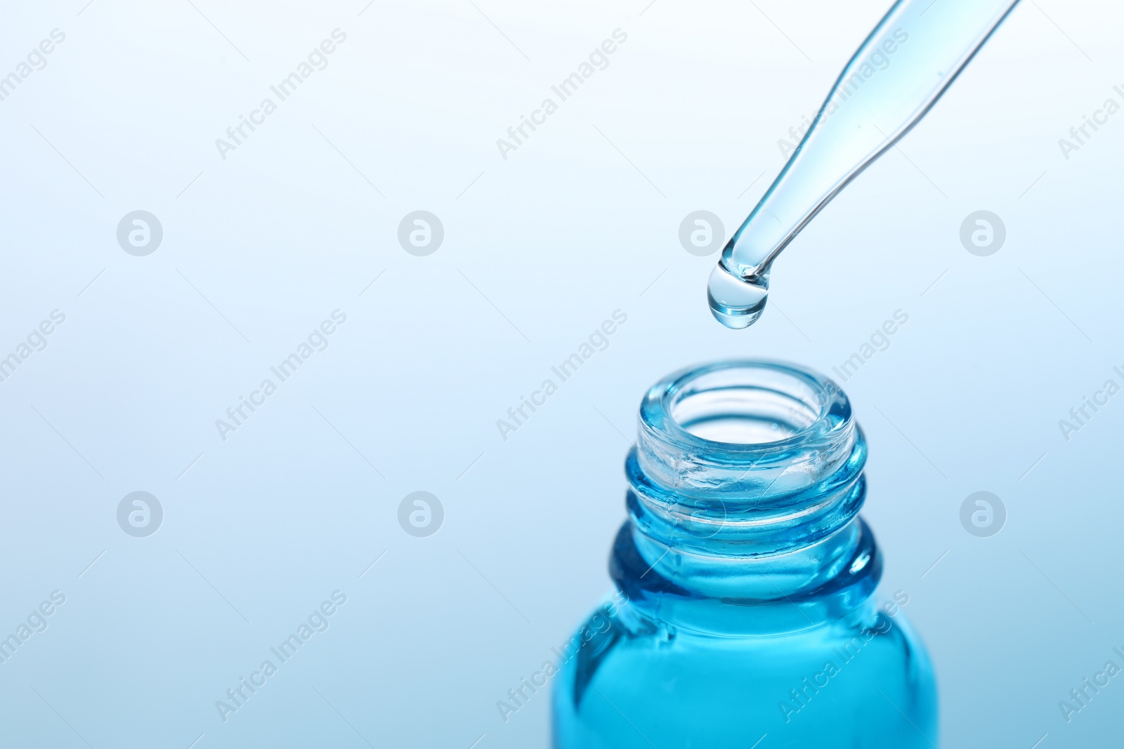 Photo of Dripping liquid from pipette into glass bottle on light blue background, closeup. Space for text