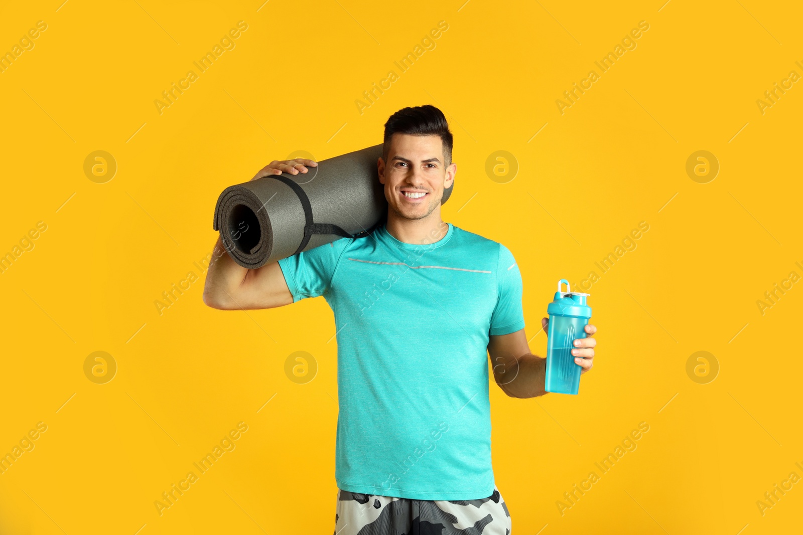 Photo of Handsome man with yoga mat and shaker on yellow background