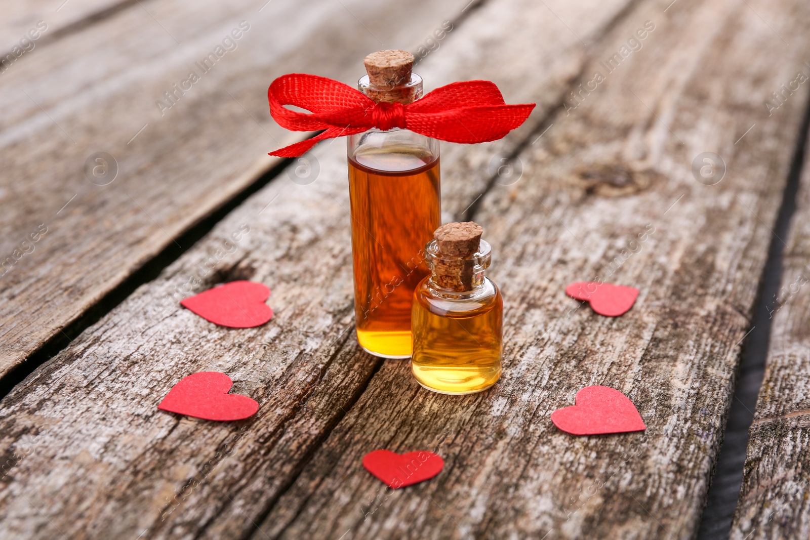 Photo of Bottles of love potion and paper hearts on wooden table