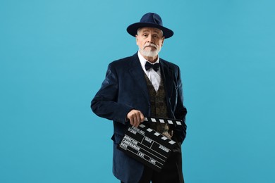 Senior actor with clapperboard on light blue background. Film industry