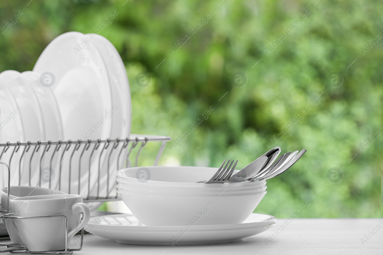 Photo of Set of clean dishes, cups and cutlery on table against blurred background. Space for text