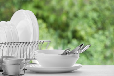 Photo of Set of clean dishes, cups and cutlery on table against blurred background. Space for text