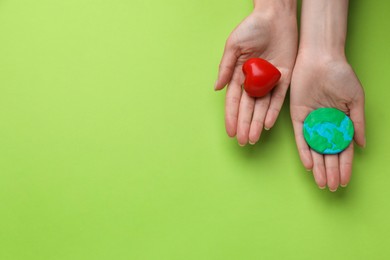 Photo of Woman holding model of planet and red heart on green background, top view with space for text. Earth Day