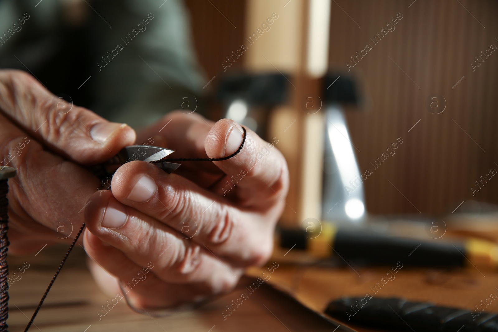 Photo of Man cutting thread while working with leather at table, closeup