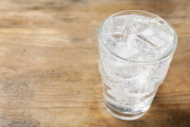 Photo of Glass of soda water with ice on wooden table. Space for text
