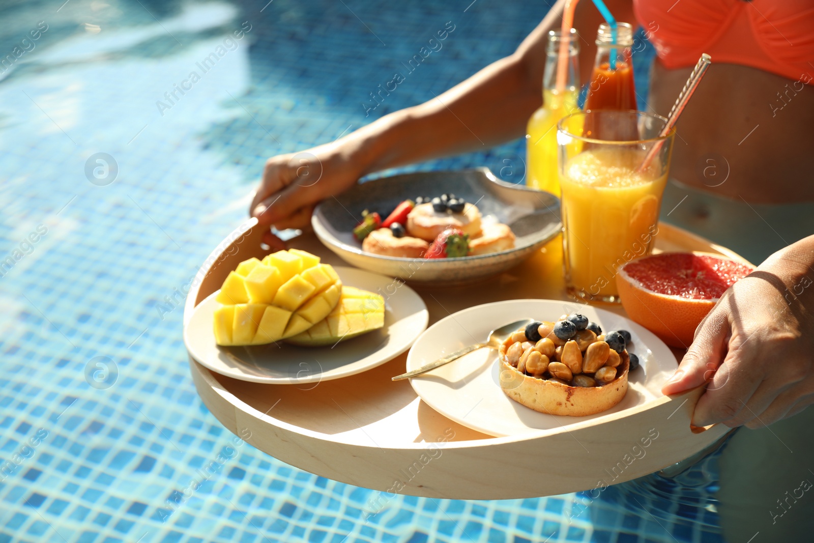 Photo of Young woman with delicious breakfast on floating tray in swimming pool, closeup