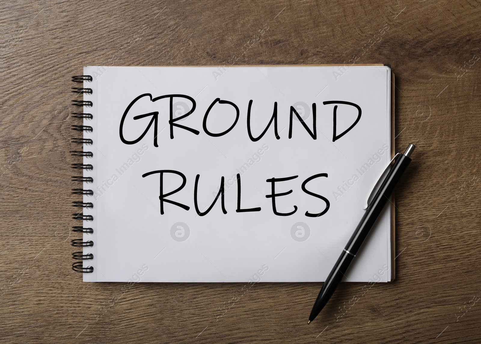 Image of Notebook with text GROUND RULES and pen on wooden table, top view