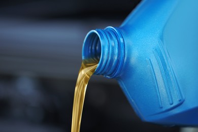 Pouring motor oil from blue container against blurred background, closeup. Space for text