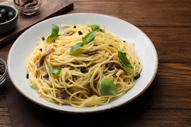 Photo of Delicious pasta with anchovies, olives and basil on wooden table
