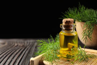 Photo of Bottle of essential oil and fresh dill on dark wooden table, closeup. Space for text