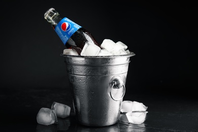 Photo of MYKOLAIV, UKRAINE - FEBRUARY 11, 2021: Glass bottle of Pepsi and ice cubes in bucket on black table against dark background